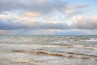 Fırtınadan sonra Baltık Denizi. Dramatik gökyüzü, parlayan bulutlar, yumuşak güneş ışığı. Dalgalar, su sıçratma. Resimli manzara, deniz manzarası, doğa. Panoramik görünüm