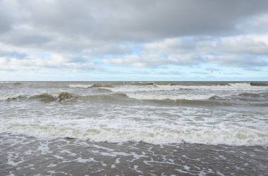 Fırtınadan sonra Baltık Denizi. Dramatik gökyüzü, parlayan bulutlar, yumuşak güneş ışığı. Dalgalar, su sıçratma. Resimli manzara, deniz manzarası, doğa. Panoramik görünüm