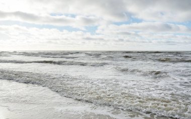 Fırtınadan sonra Baltık Denizi. Dramatik gökyüzü, parlayan bulutlar, yumuşak güneş ışığı. Dalgalar, su sıçratma. Resimli manzara, deniz manzarası, doğa. Panoramik görünüm