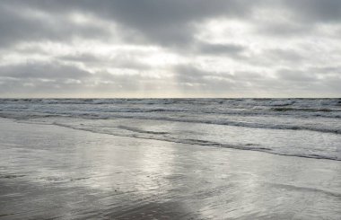 Kumlu sahilden Baltık denizinin panoramik görüntüsü (kum tepeleri). Parlak bulutlu dramatik bir gökyüzü. Dalgalar, su sıçramaları. Idyllic deniz manzarası. Bahar havası, iklim değişikliği, doğa