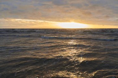 Fırtınadan sonra gün batımında Baltık Denizi. Dramatik gökyüzü, parlayan bulutlar, dofty altın güneş ışığı, dalgalar, fışkıran su. Resimli panoramik manzara. Doğa, çevre, ekoloji