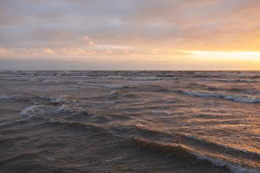 Fırtınadan sonra gün batımında Baltık Denizi. Dramatik gökyüzü, parlayan bulutlar, dofty altın güneş ışığı, dalgalar, fışkıran su. Resimli panoramik manzara. Doğa, çevre, ekoloji