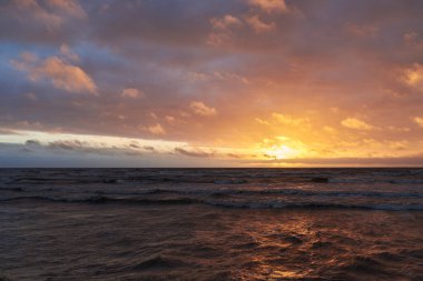 Fırtınadan sonra gün batımında Baltık Denizi. Dramatik gökyüzü, parlayan bulutlar, dofty altın güneş ışığı, dalgalar, fışkıran su. Resimli panoramik manzara. Doğa, çevre, ekoloji