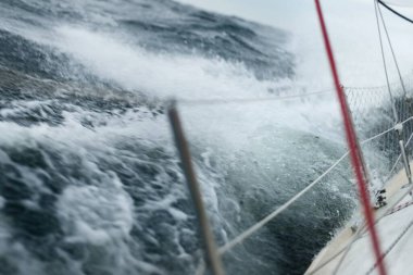 Açık denizde yelken açan topuklu bir yat. Güverte ve donanım görüntüsü. Karanlık fırtına dalgaları, su sıçramaları. Uzun pozlama, hareket. Kötü hava, kasırga, tehlike. Yarış, yarış, spor