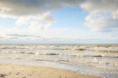 Kumlu bir sahilden (kum tepeleri) Baltık denizinin panoramik görüntüsü. Parlayan bulutlarla, dalgalarla ve su sıçramalarıyla berrak bir gökyüzü. Idyllic deniz manzarası. Sıcak kış havası, iklim değişikliği, doğa