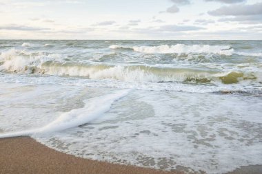 Gün batımında Baltık kıyıları (kum tepeleri). Yumuşak güneş ışığı, parlayan bulutlar, dalgalar ve su fışkıran berrak gökyüzü. Idyllic deniz manzarası. Liepaja, Letonya, Avrupa. Sıcak kış havası, iklim değişikliği, doğa