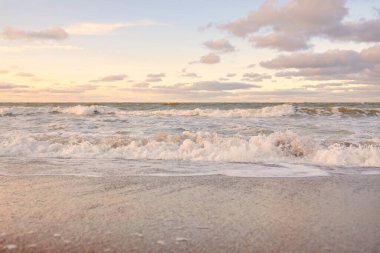 Gün batımında Baltık kıyıları (kum tepeleri). Yumuşak güneş ışığı, parlayan bulutlar, dalgalar ve su fışkıran berrak gökyüzü. Idyllic deniz manzarası. Liepaja, Letonya, Avrupa. Sıcak kış havası, iklim değişikliği, doğa