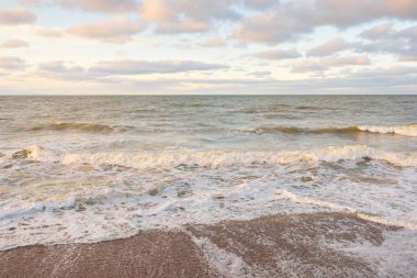 Gün batımında Baltık kıyıları (kum tepeleri). Yumuşak güneş ışığı, parlayan bulutlar, dalgalar ve su fışkıran berrak gökyüzü. Idyllic deniz manzarası. Liepaja, Letonya, Avrupa. Sıcak kış havası, iklim değişikliği, doğa