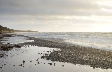 Gün batımında Baltık kıyılarından panoramik manzara. Dramatik bulutlar, parlayan bulutlar, fırtınadan sonra altın güneş ışığı. Doğa, çevre, iklim değişikliği, kararsız hava