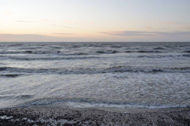 Gün batımında Baltık Denizi. Dramatik gökyüzü, mavi ve pembe parlayan bulutlar, altın güneş ışığı. Dalgalar, su sıçratma. Resimli manzara, deniz manzarası, doğa. Panoramik görünüm,