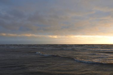 Fırtınadan sonra gün batımında Baltık Denizi. Dramatik gökyüzü, parlayan bulutlar, dofty altın güneş ışığı, dalgalar, fışkıran su. Resimli panoramik manzara. Doğa, çevre, ekoloji