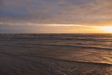 Fırtınadan sonra gün batımında Baltık Denizi. Dramatik gökyüzü, parlayan bulutlar, dofty altın güneş ışığı, dalgalar, fışkıran su. Resimli panoramik manzara. Doğa, çevre, ekoloji