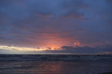 Fırtınadan sonra gün batımında Baltık Denizi. Dramatik gökyüzü, parlayan bulutlar, dofty altın güneş ışığı, dalgalar, fışkıran su. Resimli panoramik manzara. Doğa, çevre, ekoloji