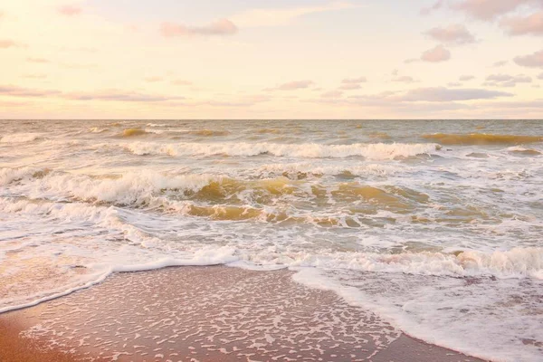 Gün batımında Baltık kıyıları (kum tepeleri). Yumuşak güneş ışığı, parlayan bulutlar, dalgalar ve su fışkıran berrak gökyüzü. Idyllic deniz manzarası. Liepaja, Letonya, Avrupa. Sıcak kış havası, iklim değişikliği, doğa