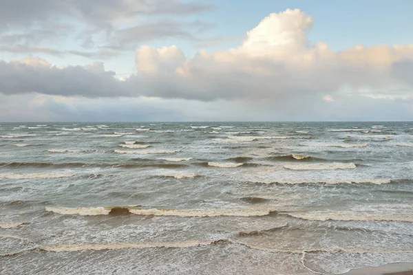 Fırtınadan sonra Baltık Denizi. Dramatik gökyüzü, parlayan bulutlar, yumuşak güneş ışığı. Dalgalar, su sıçratma. Resimli manzara, deniz manzarası, doğa. Panoramik görünüm
