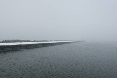 Kumlu sahilden Baltık Denizi 'nin panoramik manzarası. Deniz fenerine dolaş, dalgalar. Yoğun beyaz sis, sis, kar. Dalgalar, su sıçramaları. Deniz Burnu. Tek renkli kış manzarası