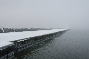 Kumlu sahilden Baltık Denizi 'nin panoramik manzarası. Deniz fenerine dolaş, dalgalar. Yoğun beyaz sis, sis, kar. Dalgalar, su sıçramaları. Deniz Burnu. Tek renkli kış manzarası