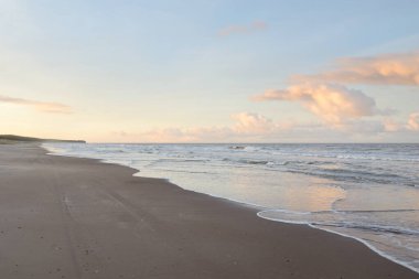 Gün batımında Baltık kıyıları (kum tepeleri). Yumuşak güneş ışığı, parlayan bulutlar, dalgalar ve su fışkıran berrak gökyüzü. Idyllic deniz manzarası. Liepaja, Letonya, Avrupa. Sıcak kış havası, iklim değişikliği, doğa