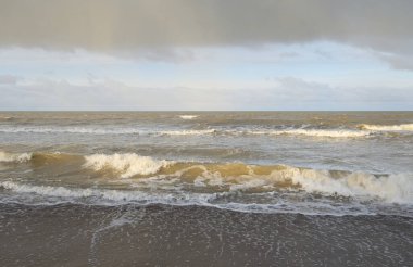 Kumlu bir sahilden (kum tepeleri) Baltık denizinin panoramik görüntüsü. Koyu bulutlu dramatik bir gökyüzü. Dalgalar, su sıçramaları. Idyllic deniz manzarası. Sıcak kış havası, iklim değişikliği, doğa. Danimarka