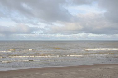 Kumlu bir sahilden (kum tepeleri) Baltık denizinin panoramik görüntüsü. Koyu bulutlu dramatik bir gökyüzü. Dalgalar, su sıçramaları. Idyllic deniz manzarası. Sıcak kış havası, iklim değişikliği, doğa. Danimarka