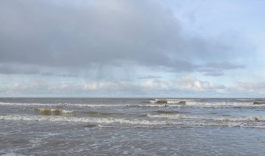 Kumlu bir sahilden (kum tepeleri) Baltık denizinin panoramik görüntüsü. Koyu bulutlu dramatik bir gökyüzü. Dalgalar, su sıçramaları. Idyllic deniz manzarası. Sıcak kış havası, iklim değişikliği, doğa. Danimarka