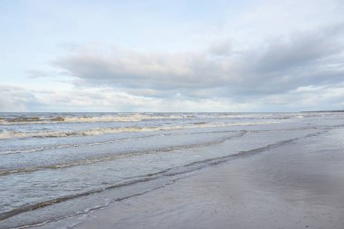 Kumlu bir sahilden (kum tepeleri) Baltık denizinin panoramik görüntüsü. Koyu bulutlu dramatik bir gökyüzü. Dalgalar, su sıçramaları. Idyllic deniz manzarası. Sıcak kış havası, iklim değişikliği, doğa. Danimarka