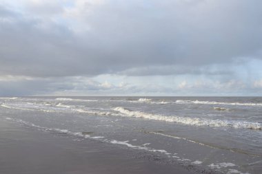 Kumlu bir sahilden (kum tepeleri) Baltık denizinin panoramik görüntüsü. Koyu bulutlu dramatik bir gökyüzü. Dalgalar, su sıçramaları. Idyllic deniz manzarası. Sıcak kış havası, iklim değişikliği, doğa. Danimarka