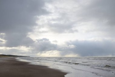 Gün batımında Baltık kıyıları (kum tepeleri). Yumuşak güneş ışığı, parlayan bulutlar, dalgalar ve su fışkıran berrak gökyüzü. Idyllic deniz manzarası. Liepaja, Letonya, Avrupa. Sıcak kış havası, iklim değişikliği, doğa