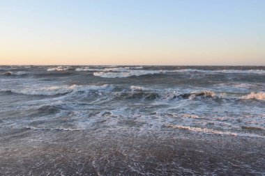 Gün batımında Baltık kıyısı. Yumuşak altın güneş ışığı, parlayan gökyüzü, dalgalar. Idyllic deniz manzarası. Seyahat yerleri, eko turizm, doğa, hava durumu, iklim değişikliği. Resimli panoramik manzara