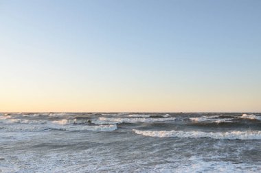 Gün batımında Baltık kıyısı. Yumuşak altın güneş ışığı, parlayan gökyüzü, dalgalar. Idyllic deniz manzarası. Seyahat yerleri, eko turizm, doğa, hava durumu, iklim değişikliği. Resimli panoramik manzara