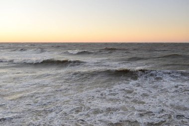 Gün batımında Baltık kıyısı. Yumuşak altın güneş ışığı, parlayan gökyüzü, dalgalar. Idyllic deniz manzarası. Seyahat yerleri, eko turizm, doğa, hava durumu, iklim değişikliği. Resimli panoramik manzara