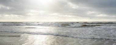 Kumlu sahilden Baltık denizinin panoramik görüntüsü (kum tepeleri). Parlak bulutlu dramatik bir gökyüzü. Dalgalar, su sıçramaları. Idyllic deniz manzarası. Bahar havası, iklim değişikliği, doğa