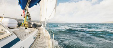 Teknelerle donatılmış modern bir yat. Tahta meşe güverteli. Clyde Nehri Firth 'ün kayalık kıyılarına doğru yol alıyorlar. Dramatik bir gökyüzü. İskoçya, İngiltere. Seyahat yerleri, eko turizm, tatiller, saf doğa.