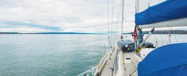 Bulutlu bir günde, Jura adasının kayalık kıyılarında seyir halindeki ahşap meşe güvertesiyle donatılmış modern bir yat. Inner Hebrides, İskoçya, İngiltere. Spor, eğlence, gezi, seyahat yerleri.