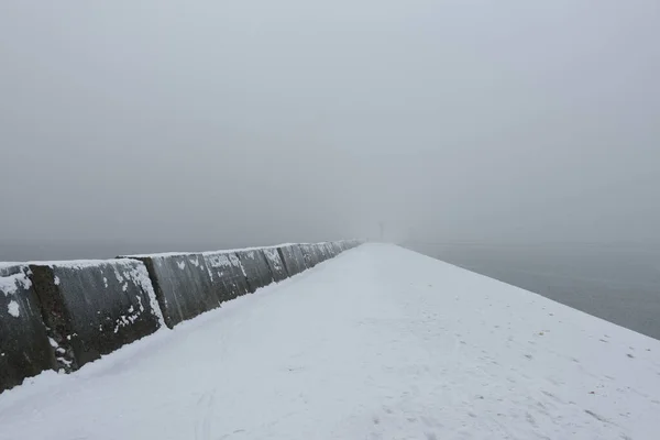 砂浜の海岸からバルト海のパノラマビュー 灯台への遊歩道 防波堤 厚い白い霧 水のスプラッシュ シースケープ モノクローム冬景色 — ストック写真