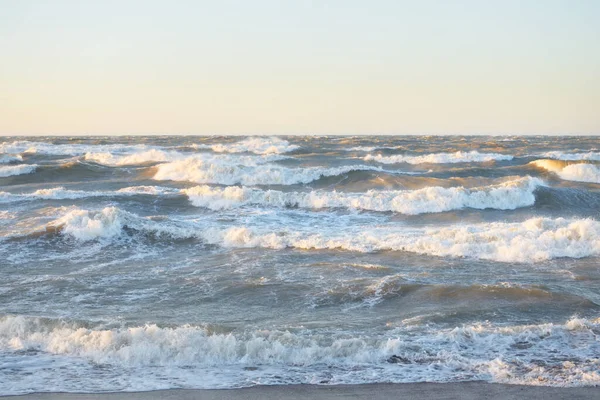 Gün batımında Baltık kıyısı. Yumuşak altın güneş ışığı, parlayan gökyüzü, dalgalar. Idyllic deniz manzarası. Seyahat yerleri, eko turizm, doğa, hava durumu, iklim değişikliği. Resimli panoramik manzara