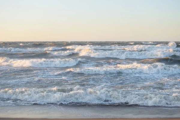 Gün batımında Baltık kıyısı. Yumuşak altın güneş ışığı, parlayan gökyüzü, dalgalar. Idyllic deniz manzarası. Seyahat yerleri, eko turizm, doğa, hava durumu, iklim değişikliği. Resimli panoramik manzara