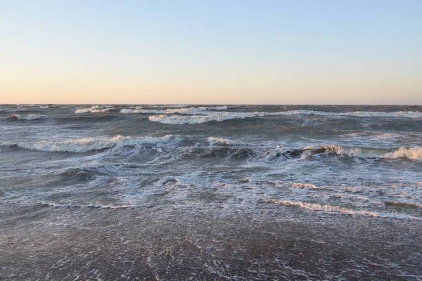 Gün batımında Baltık kıyısı. Yumuşak altın güneş ışığı, parlayan gökyüzü, dalgalar. Idyllic deniz manzarası. Seyahat yerleri, eko turizm, doğa, hava durumu, iklim değişikliği. Resimli panoramik manzara