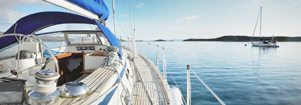 Sloop rigged modern yacht with wooden teak deck sailing near the shore of Jura island on a sunny day. Cloudy blue sky. Reflections on the water. Inner Hebrides, Scotland, UK