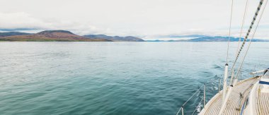 Bulutlu bir günde, Jura adasının kayalık kıyılarında seyir halindeki ahşap meşe güvertesiyle donatılmış modern bir yat. Inner Hebrides, İskoçya, İngiltere. Spor, eğlence, gezi, seyahat yerleri.