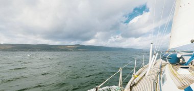 Teknelerle donatılmış modern bir yat. Tahta meşe güverteli. Clyde Nehri Firth 'ün kayalık kıyılarına doğru yol alıyorlar. Dramatik bir gökyüzü. İskoçya, İngiltere. Seyahat yerleri, eko turizm, tatiller, saf doğa.