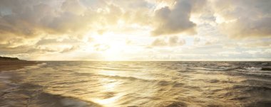 Gün batımında fırtınadan sonra Baltık Denizi kıyısında parlayan kümülüs bulutlarıyla açık bir gökyüzü. Dramatik bulut manzarası. Yumuşak altın güneş ışığı. Resimli bir manzara var. Hava kararsız. Uzun pozlama