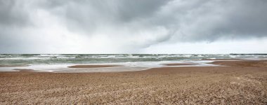 Fırtına sonrası dramatik bulutların altında Baltık Denizi 'nin kumlu sahili. Letonya 'da sızıntı var. Destansı deniz manzarası. Kasırga, fırtına, sert hava, meteoroloji, iklim değişikliği, doğal fenomen