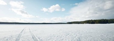 Gün batımında donmuş göl ve çam ormanı. Buz dokusu. Traktör izleri yakın plan. Dramatik mavi gökyüzü, bulutlu manzara. Kış Harikalar Diyarı. Doğa, ekoloji, iklim değişikliği, eko-turizm, kararsız hava