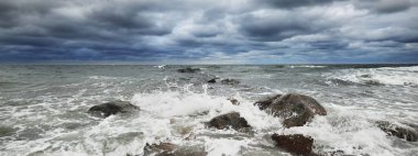 Baltık Denizi üzerinde kara fırtına bulutları. Kiel, Almanya. Kayalar, dalgalar ve su yakından sıçrıyor. İskeleden bir manzara. Döneklik havası, iklim teması. Doğa, turizm, gezi, eğlence