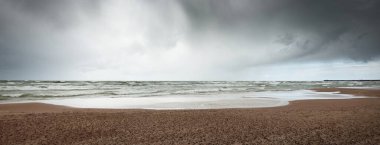 Fırtına sonrası dramatik bulutların altında Baltık Denizi 'nin kumlu sahili. Letonya 'da sızıntı var. Destansı deniz manzarası. Kasırga, fırtına, sert hava, meteoroloji, iklim değişikliği, doğal fenomen