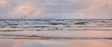 Kumlu bir sahilden Baltık Denizi 'nin panoramik manzarası. Açık günbatımı gökyüzü, parlak pembe bulutlar, yumuşak ışık. Suyun simetri yansımaları, doğal ayna. Hava, kış, iklim değişikliği, doğa