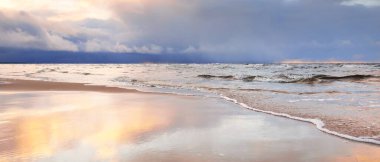 Kumlu bir sahilden Baltık Denizi 'nin panoramik manzarası. Açık günbatımı gökyüzü, parlak pembe bulutlar, yumuşak ışık. Suyun simetri yansımaları, doğal ayna. Hava, kış, iklim değişikliği, doğa