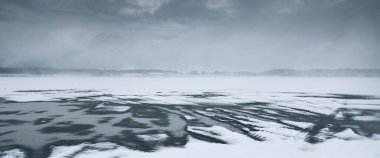 Karla kaplı tarım tarlaları ve ormanlar kar fırtınasından önce dramatik kara bulutlar altında. Traktör izleri yakın plan. Kırsal kesimde kış manzarası. Doğa, ekoloji, çevre, iklim değişikliği, küresel ısınma