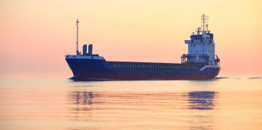 Büyük bir kargo gemisi gün batımında Baltık Denizi 'ne açılacak. Yumuşak altın güneş ışığı. Deniz manzarası kavramı. Yelkenliden panoramik görüntü. Nakliye, denizcilik, lojistik.